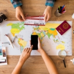 Wisatawan menyusun itinerary liburan menggunakan peta, laptop, dan buku catatan sebelum memulai perjalanan.