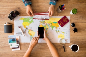 Wisatawan menyusun itinerary liburan menggunakan peta, laptop, dan buku catatan sebelum memulai perjalanan.