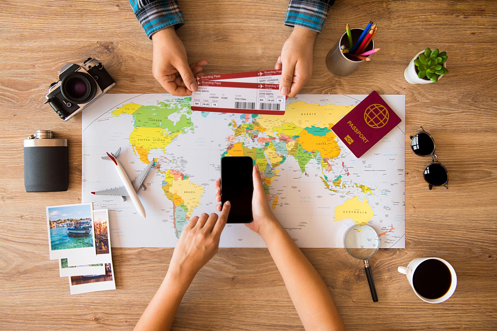 Wisatawan menyusun itinerary liburan menggunakan peta, laptop, dan buku catatan sebelum memulai perjalanan.