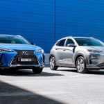 Perbandingan mobil hybrid dan mobil listrik yang diparkir berdampingan, dengan mobil listrik sedang mengisi daya di charging station.