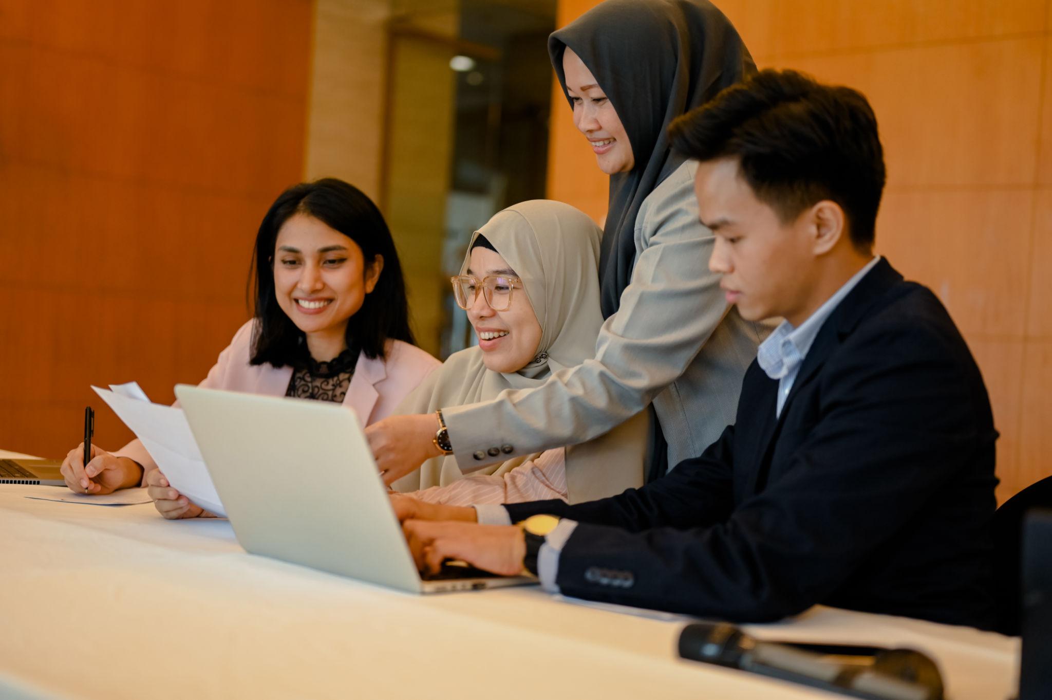Sekelompok profesional muda berdiskusi di kantor menggunakan laptop sebagai ilustrasi hard skill dan soft skill di dunia kerja.
