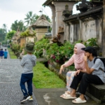 Keluarga Indonesia menikmati liburan di destinasi wisata dengan koper dan ransel sebagai ilustrasi tips liburan hemat.