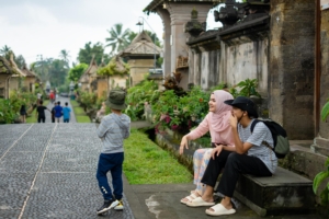 Keluarga Indonesia menikmati liburan di destinasi wisata dengan koper dan ransel sebagai ilustrasi tips liburan hemat.