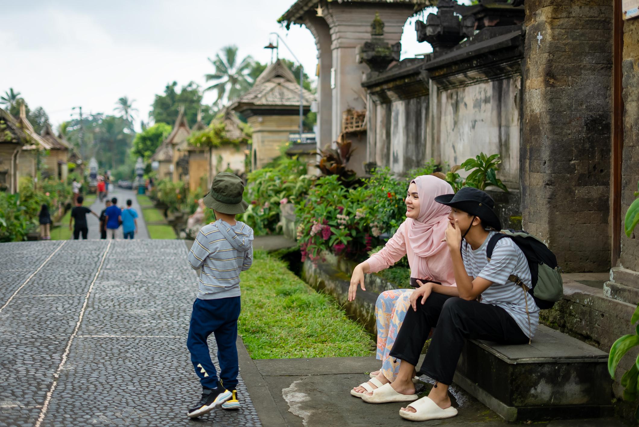 Keluarga Indonesia menikmati liburan di destinasi wisata dengan koper dan ransel sebagai ilustrasi tips liburan hemat.